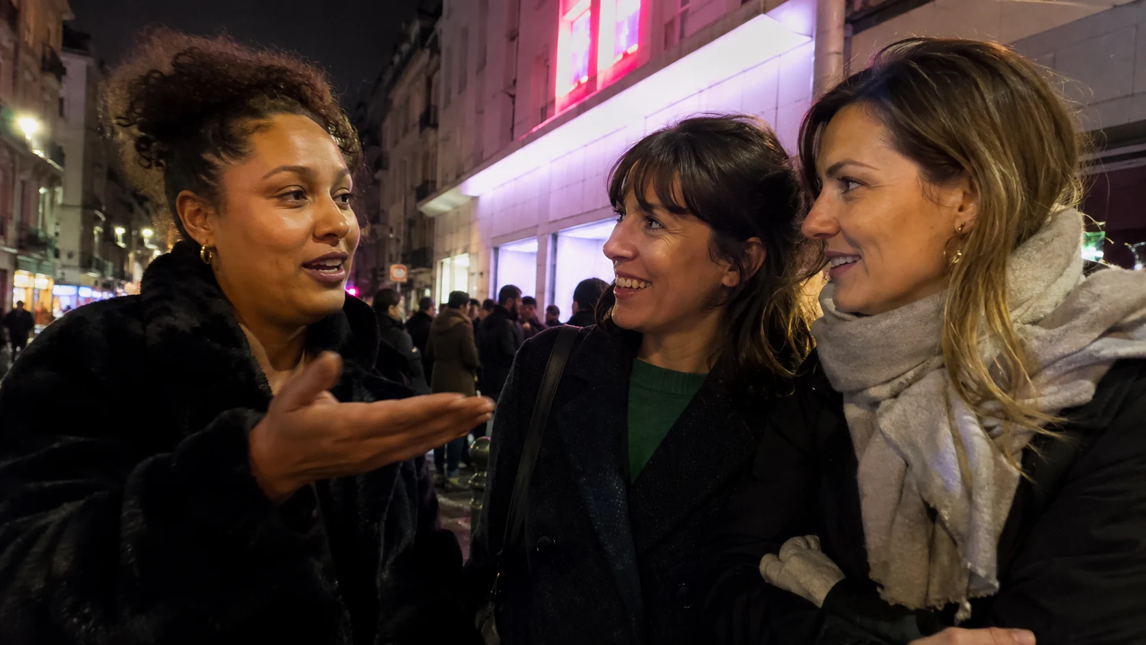 Trois amies échangent en sortant d’un cinéma de quartier le soir