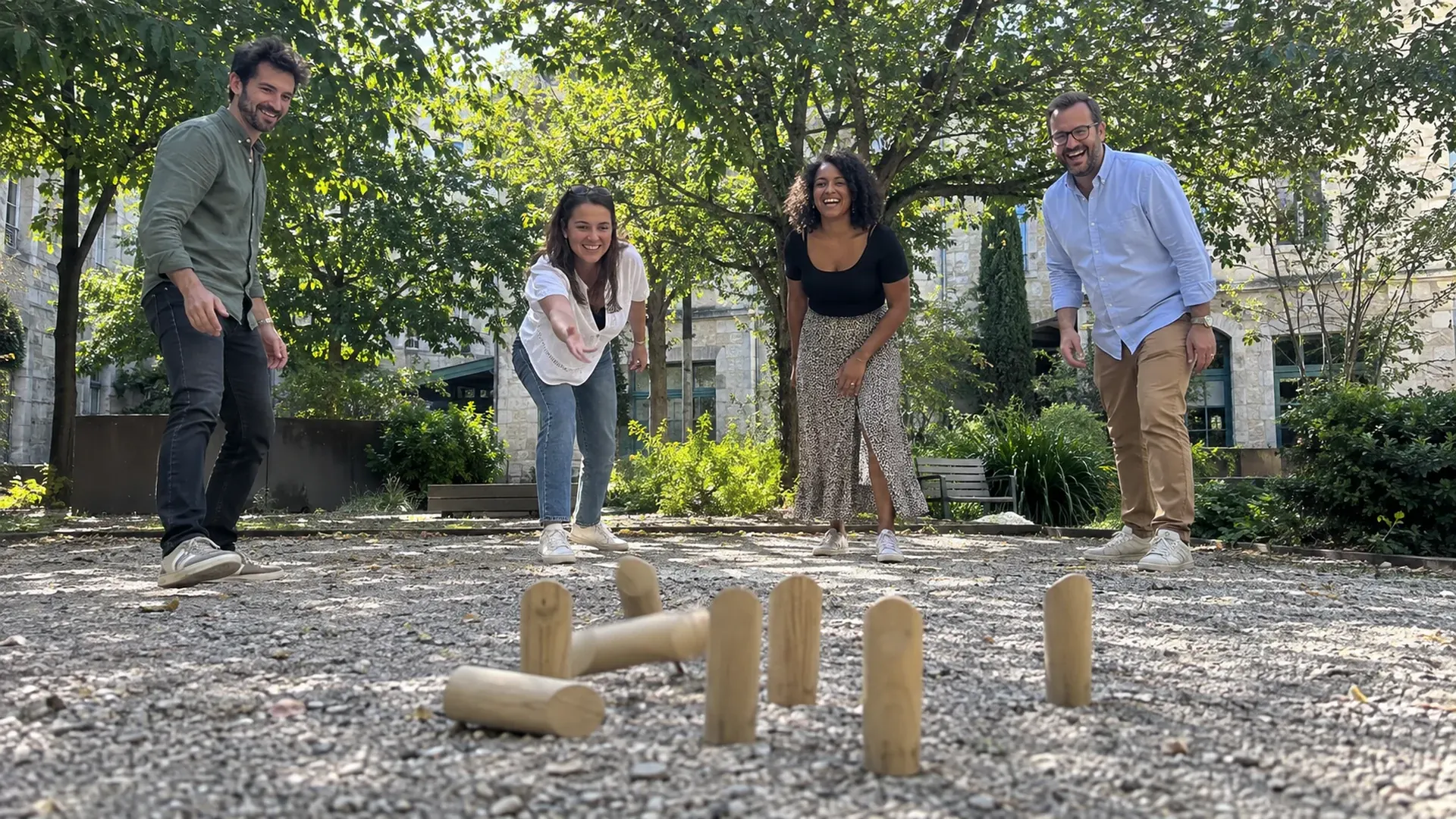 Quatre collègues jouent au mölkky dans une cour végétalisée pendant leur pause